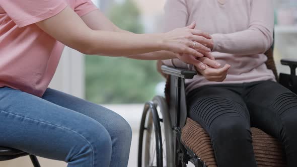 Unrecognizable Young Paralyzed Woman and Friend Holding Hands Sitting Indoors