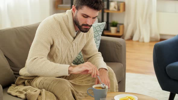 Sick Young Man in Blanket Drinking Hot Tea at Home