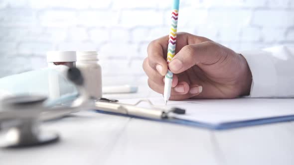 Doctor Hand Writing Prescription on Desk Close Up