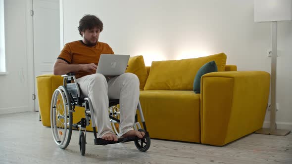 Man Freelancer Sitting on Wheelchair and Working at Home Using a Laptop