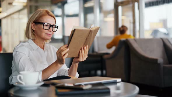 Intelligent Businesswoman Enjoying Book Reading in Cafe During Coffee Break