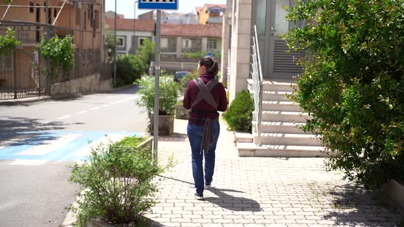 Mom with a Newborn in a Sling Walks Along the Pavement in the City