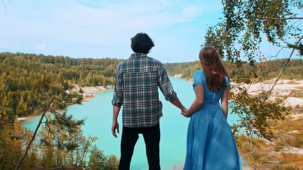 Young Happy Couple Holding Hands and Looking on a Landscape of Blue Lake and Forest