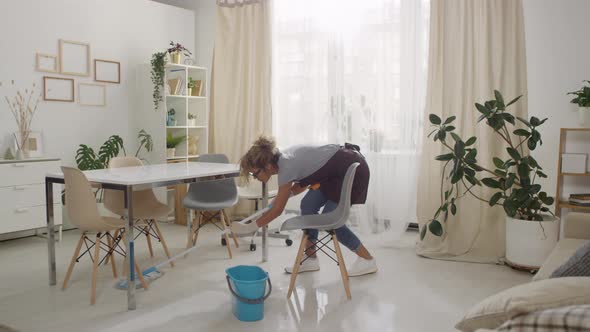 Woman Mopping Floor under Chairs in Living Room