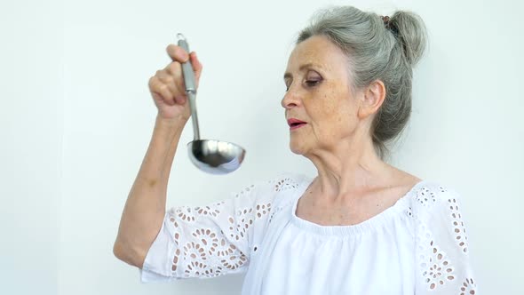 Emotional Senior Woman with Silver Hair is Holding Metal Ladle or Scoop on White Background Happy