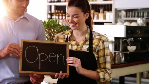 Man and waitress holding chalkboard with open sign