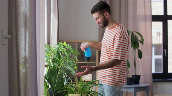 Happy Man Spraying Houseplant with Water at Home