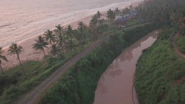 Aerial view of a river flowing near palm trees and Varkala coastline, in Kerala, India, at dusk