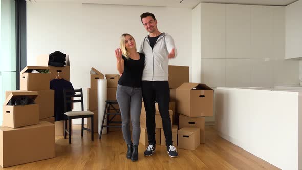 A Moving Couple Stands in an Empty Apartment and Beckons To the Camera in a Gesture of Invitation