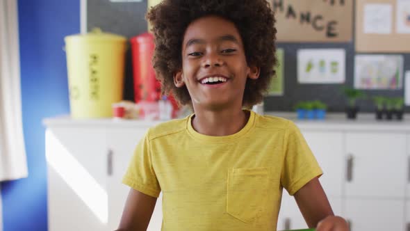 African american schoolboy standing, smiling in classroom looking at camera learning about recycling