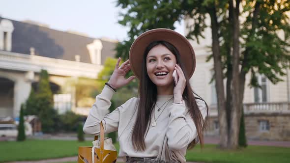 Smiling Modern Lady in Beige Hat Enjoying Her Conversation on Phone while Walking