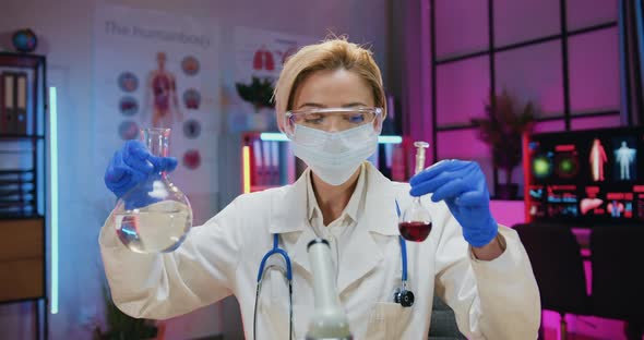 Woman Chemist in Protective Eyewear, Mask and Gloves Working with Chemical Liquids in Flasks in lab
