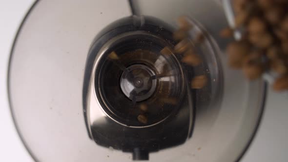 Up close overhead view of fresh, brown coffee beans being poured into fancy electric grinder for mor