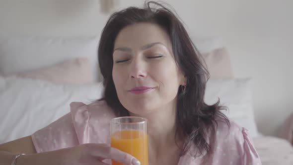 Close-up Face of Charming Caucasian Woman Drinking Orange Juice and Smiling at Camera. Positive