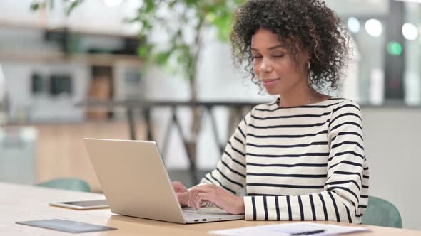Young African Woman with Laptop Smiling at Camera in Office