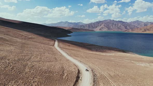 Aerial Over Off Road 4X4 Car Driving Along Gravel Trail Path Toward Lake in Arid Mountains