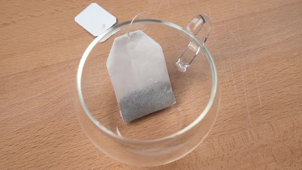 Teabag on a string with a label falls into an empty transparent cup in slow motion 