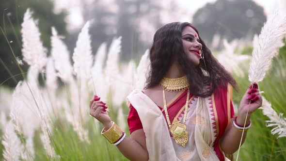 A married happy and elegant Indian woman is playing with kaash phool white flowered grass on a windy