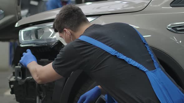 Back View of Auto Mechanic in Coronavirus Face Mask Sitting at Broken Vehicle in Repair Shop