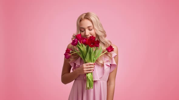 Blonde Woman Holding Smelling Bouquet Of Tulips On Pink Background