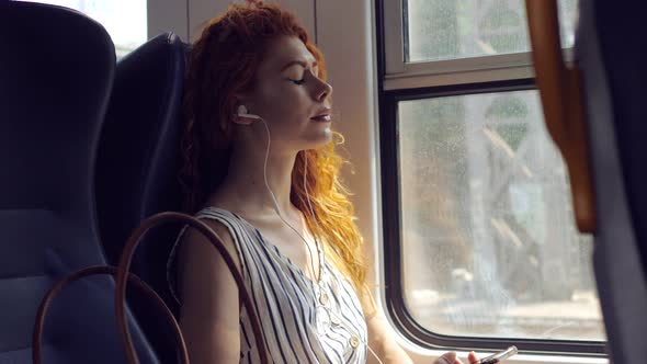 relax while traveling- woman traveling by train listens to music with headphones