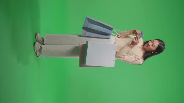 Full View Of Asian Woman With Shopping Bags Using Mobile Phone Shopping Online On Green Screen