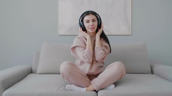 Young woman sitting on sofa listening to music with wireless headphones.