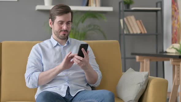 Young Man Using Smartphone on Sofa