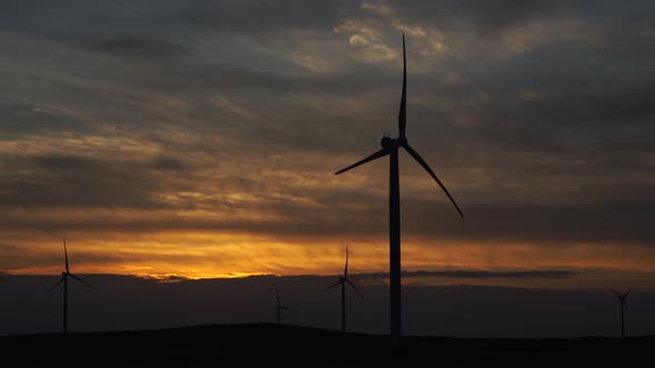 Motion the Blades of a Large Wind Turbine in a Field Against a Background of Orange Sunset on the