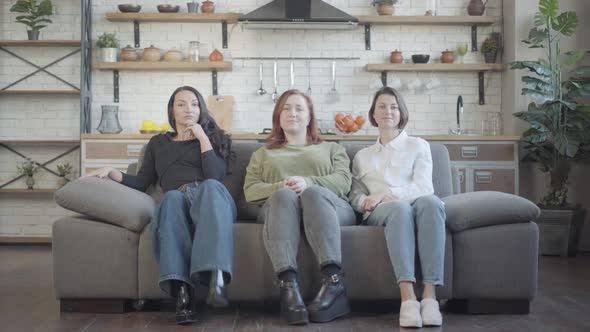 Wide Shot Portrait of Three Confident Young Caucasian Women Sitting on Couch Crossing Legs