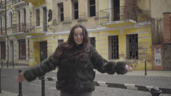 Portrait of Joyful Stylish Girl in Fur Coat and Sunglasses Having Fun on City Street. Cheerful Young