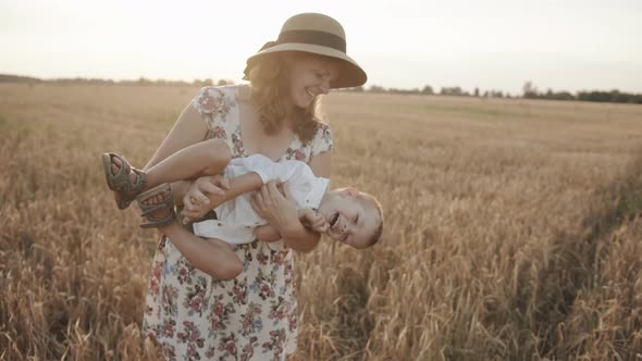 A Beautiful Young Woman in a Wheat Field Holds Her Little Son in Her Arms and Tickles Him