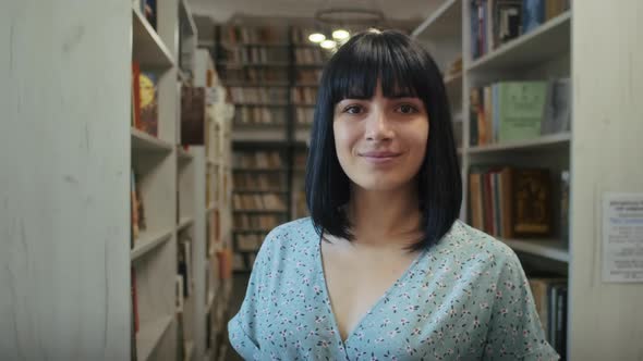 Happy Woman Reads a Book in the Library Chooses Books From the Shelf alt