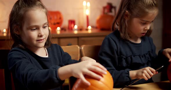 Two Cute Little Girls Are Cutting a Pumpkin on the Table for Halloween