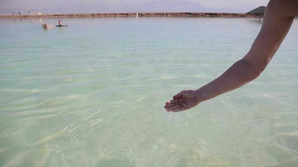 Man's hand touching sea water. Woman swimming at the background. The Dead Sea, Israel
