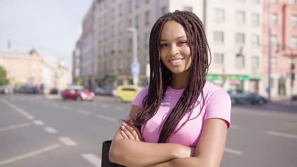 A Young Black Woman Smiles at the Camera in the Street in an Urban Area - a Busy Road