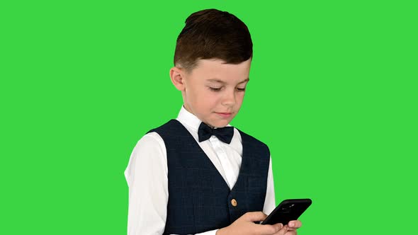 Smiling Boy in a White Shirt Bow Tie and Vest Texting on the Phone on a Green Screen Chroma Key