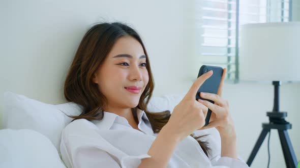 Asian attractive woman holding credit card and shopping online while lying on bed at home in morning