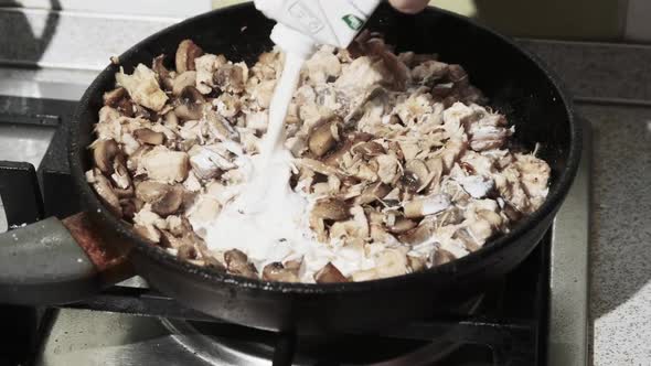 Adding Milk Cream To Fried Mushrooms in a Hot Pan at the Home Kitchen