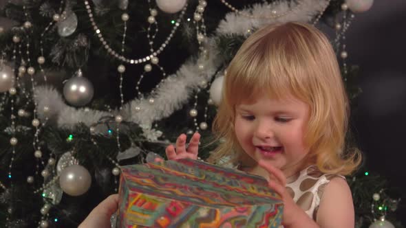 A Cute Little Girl Is Sitting Under the Christmas Tree and Opening Presents