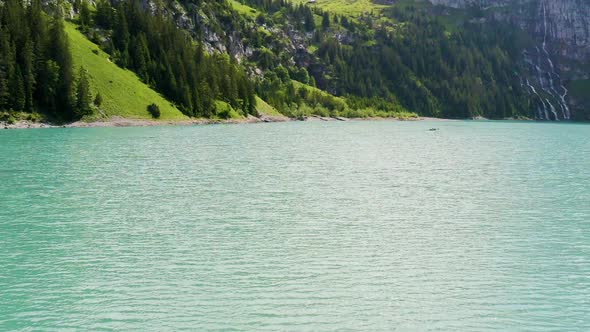 Flying low over a beautiful blue lake, tilting up and revealing stunning, green Swiss mountainscape