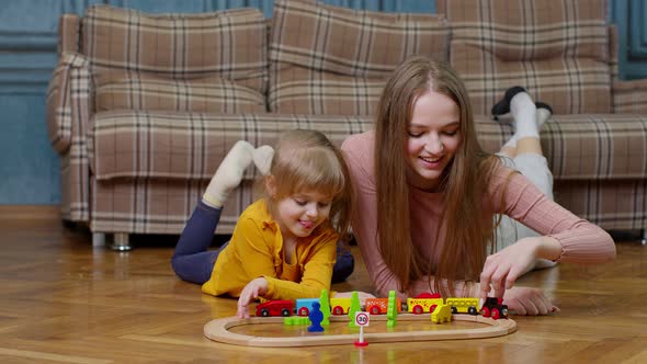 Mother with Little Daughter Child Girl Riding Toy Train on Wooden Railway Blocks Board Game at Home