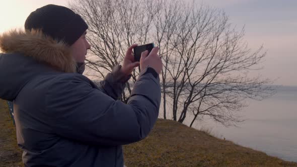 Young Man Uses a Smartphone on the Seashore Taking Pictures
