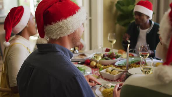 Happy caucasian man in santa hat celebrating meal with friends at christmas time