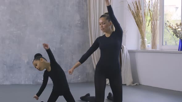 Little Asian Girl in Black Bodysuit Doing Dance Exercises with the Help of Female Trainer