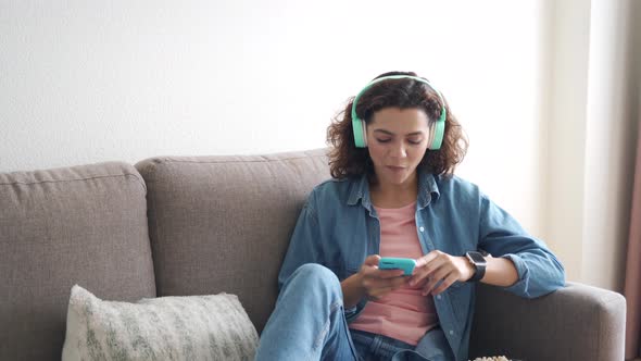 Hispanic Young Woman in Earphones Using Smartphone App Sitting at Home