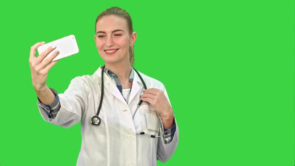 Young Pretty Female Doctor Makes Selfie on Smart Phone on a Green Screen, Chroma Key.