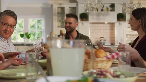 Happy caucasian parents, children and grandfather sitting at table holding hands before family meal