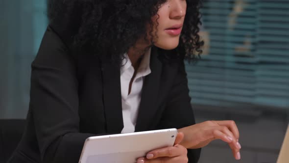 Portrait of African American Woman Views Information on a Digital Tablet and Laptop