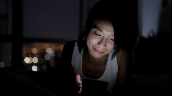 Woman using cellphone and lying on bed at night 